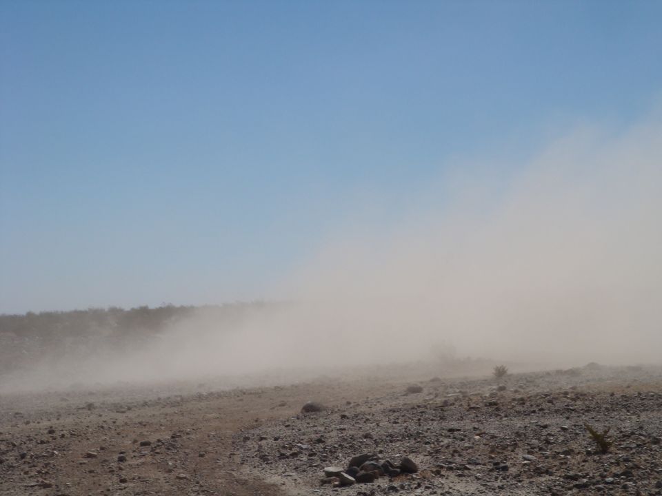 Dust cloud obscuring desert terrain under a clear blue sky