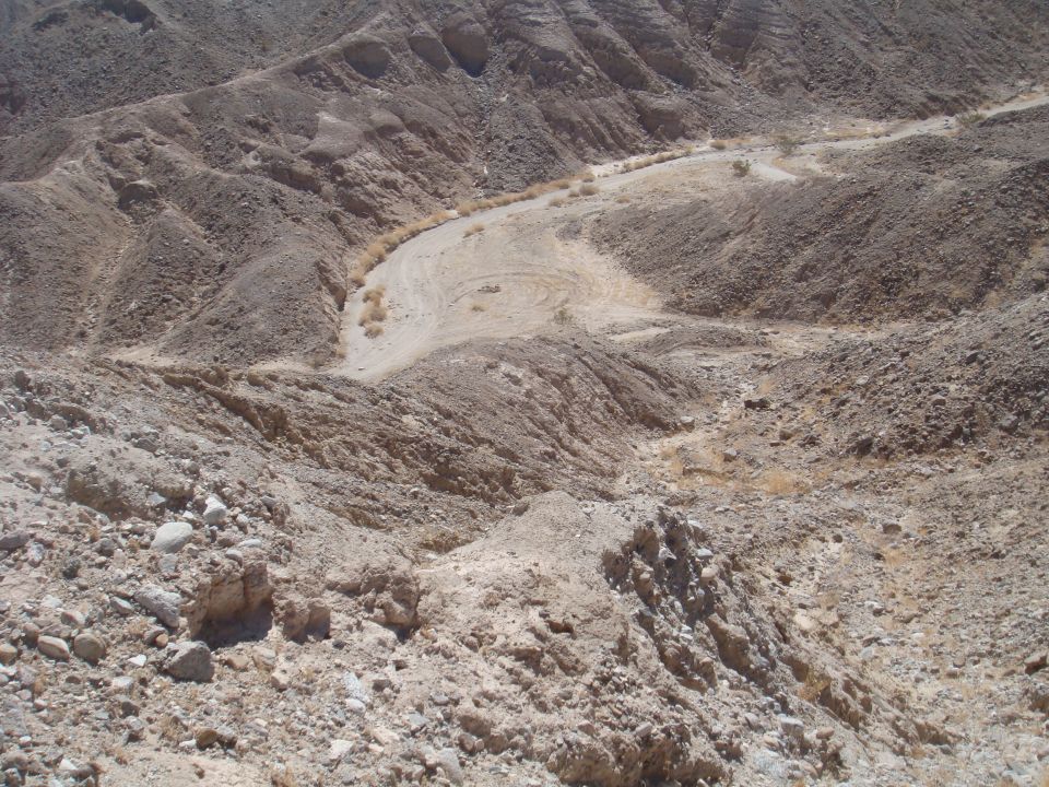 Desert canyon with a winding dirt road. A small vehicle is visible in the distance