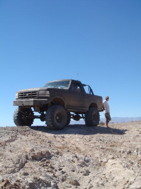 1992 Ford Bronco - A modified 1992 Ford Bronco sits on a dusty incline, its large off-road tires ready for adventure.