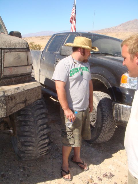 1992 Ford Bronco - Two pickup trucks are parked in a dusty, outdoor location, with two men standing nearby.