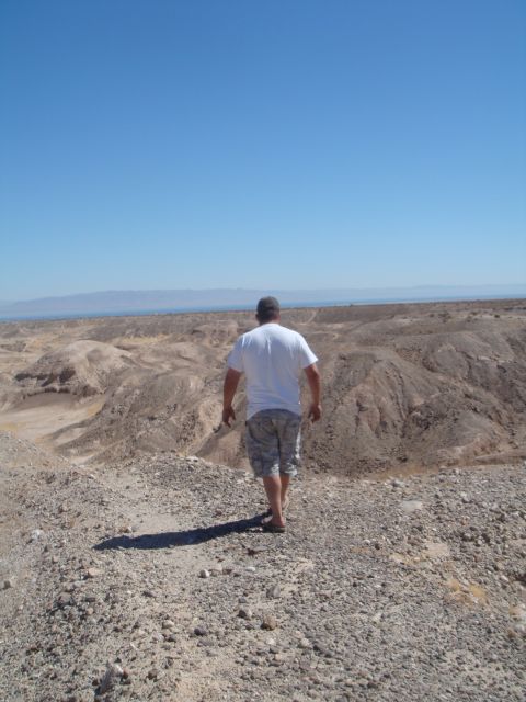 1992 Ford Bronco - A lone figure traverses a desolate desert terrain, with distant mountains under a vast sky.