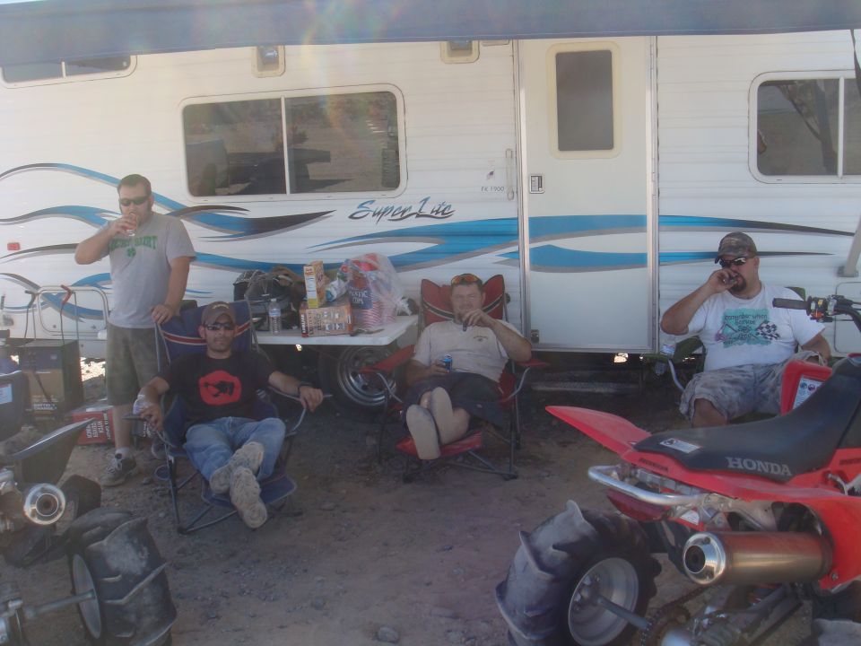 Four guys chilling outside a trailer with ATVs parked nearby