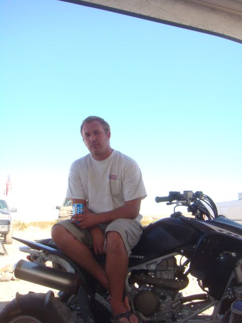1992 Ford Bronco - A man relaxes on an ATV with trucks in the distance under a clear blue sky.