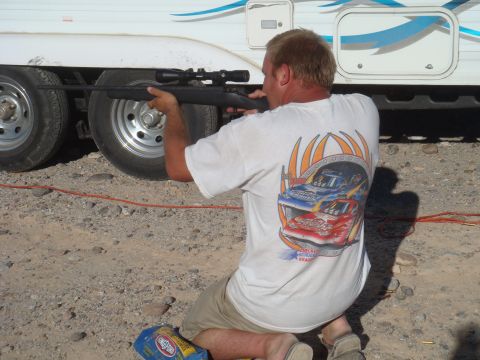 1992 Ford Bronco - A man kneels and aims a rifle towards the side of a white trailer.