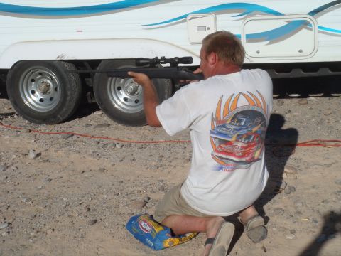 1992 Ford Bronco - A man kneels and aims a rifle towards the side of a white trailer with a blue stripe.