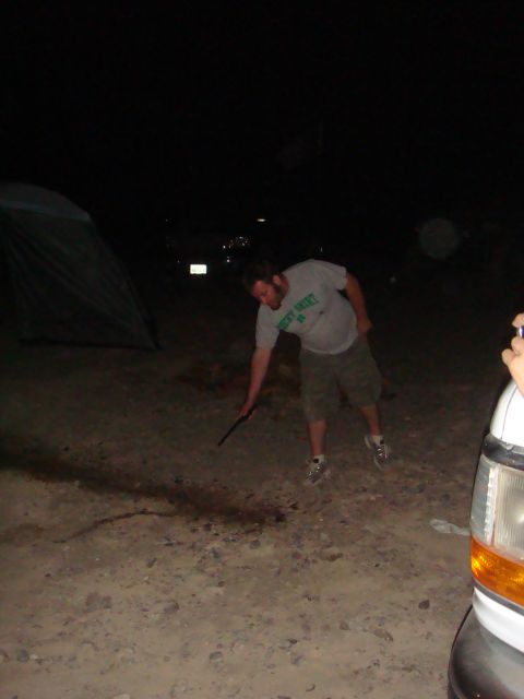 1992 Ford Bronco - Person poking the ground near a tent and the front corner of a white vehicle at night.