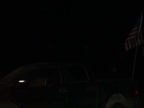 1992 Ford Bronco - Dark pickup truck with an American flag flying from a pole.
