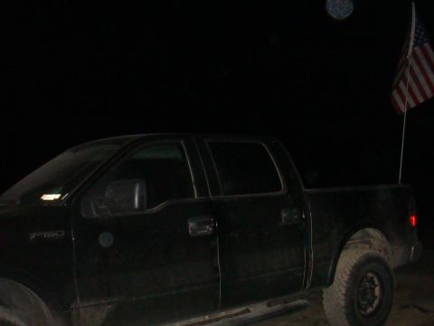 1992 Ford Bronco - A black pickup truck is seen from the side at night, with an American flag flying from its bed.