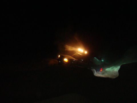 1992 Ford Bronco - A vehicle drives through the dark, its headlights and roof-mounted lights illuminating the path ahead.