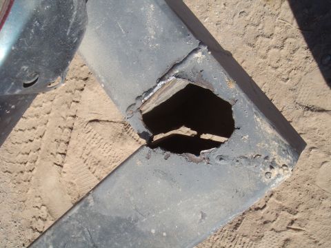 1992 Ford Bronco - A close-up view of a heavily damaged metal component, possibly a bumper or frame piece, resting on sandy terrain.