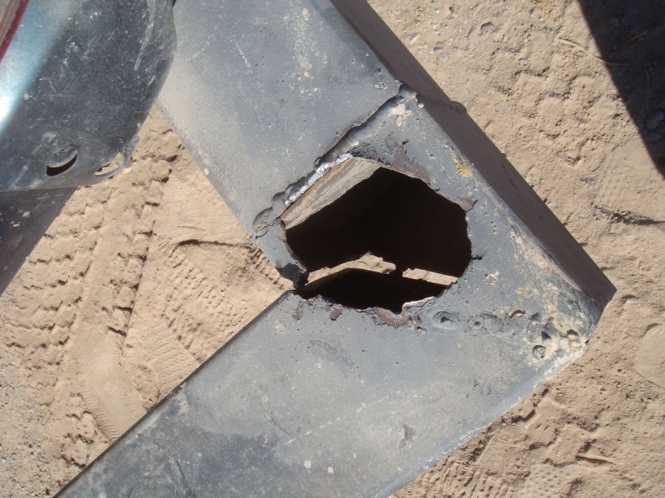 Damaged metal part with large hole, on sandy ground with tire tracks