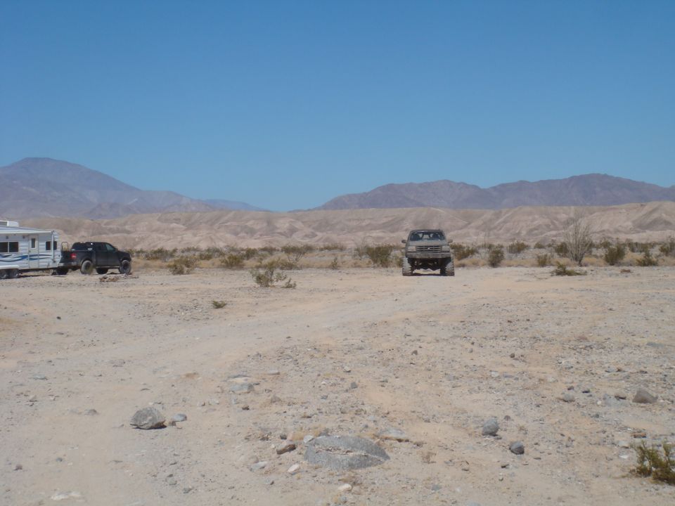 Desert scene with a lifted truck in the foreground and a trailer with a black SUV in the background