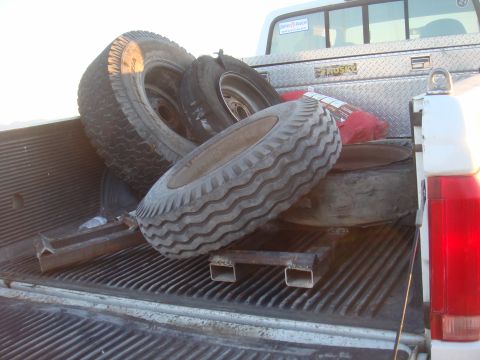 1992 Ford Bronco - A pickup truck bed is filled with tires and a toolbox, with a red bag tucked in between.