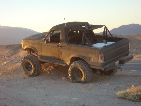 1992 Ford Bronco - A modified 1992 Ford Bronco sits on a dirt embankment under a clear sky, with mountains in the background.