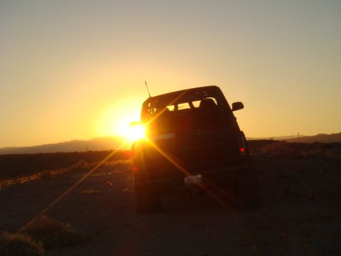 1992 Ford Bronco - A dark-colored SUV is silhouetted against a bright sunset in a desert landscape.