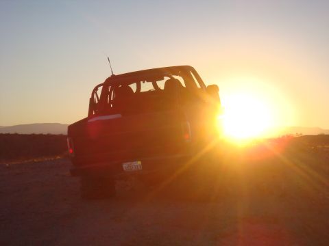 1992 Ford Bronco - A dark SUV, possibly a 1992 Ford Bronco, is seen from the rear in a desert setting as the sun sets.