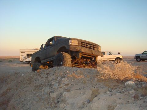 1992 Ford Bronco - A heavily modified dark SUV is shown off-roading in a desert landscape with other vehicles present.