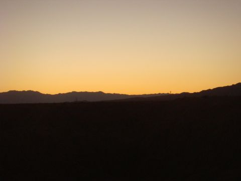 1992 Ford Bronco - The sky glows with warm colors during a desert sunset, casting silhouettes of mountains.