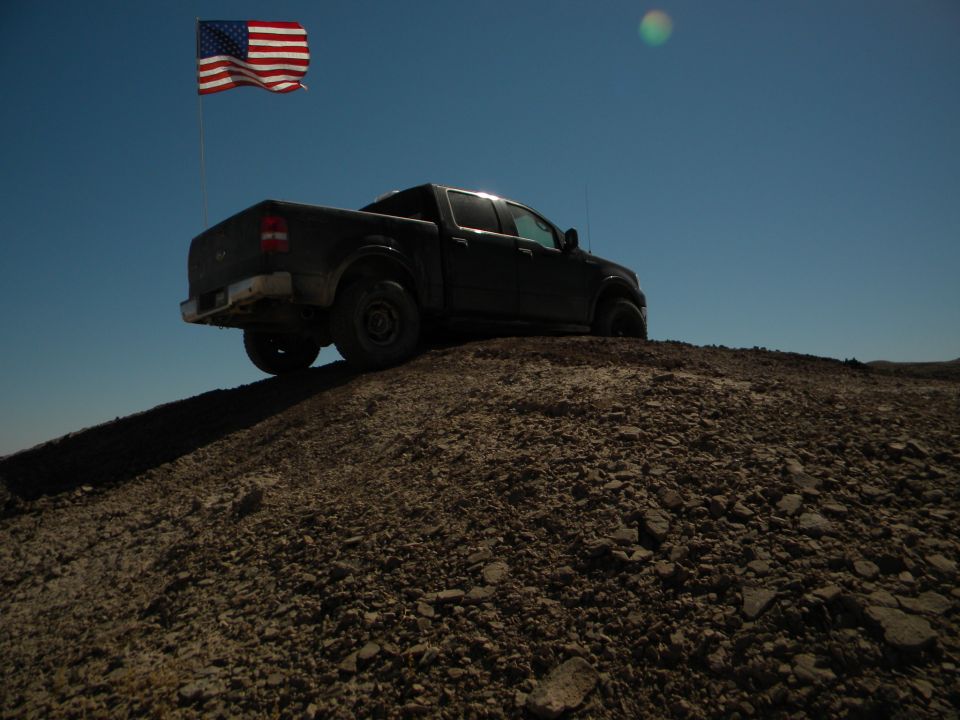 Dark pickup truck on a dirt hill with an American flag