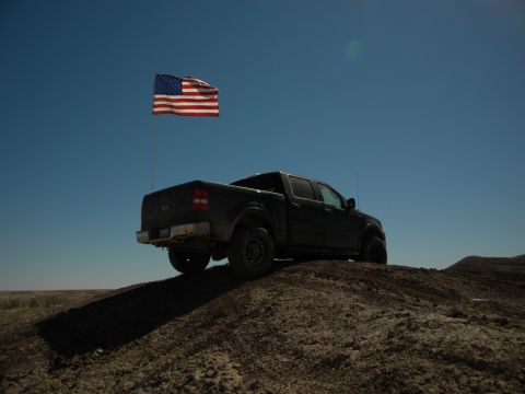1992 Ford Bronco - Pickup truck parked on a hill under a clear blue sky with an American flag.