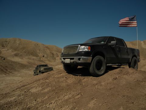 1992 Ford Bronco - Two trucks are parked on a dusty, arid landscape under a clear blue sky.