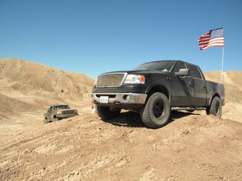 1992 Ford Bronco - Two trucks are seen off-roading in a desert landscape under a clear blue sky.
