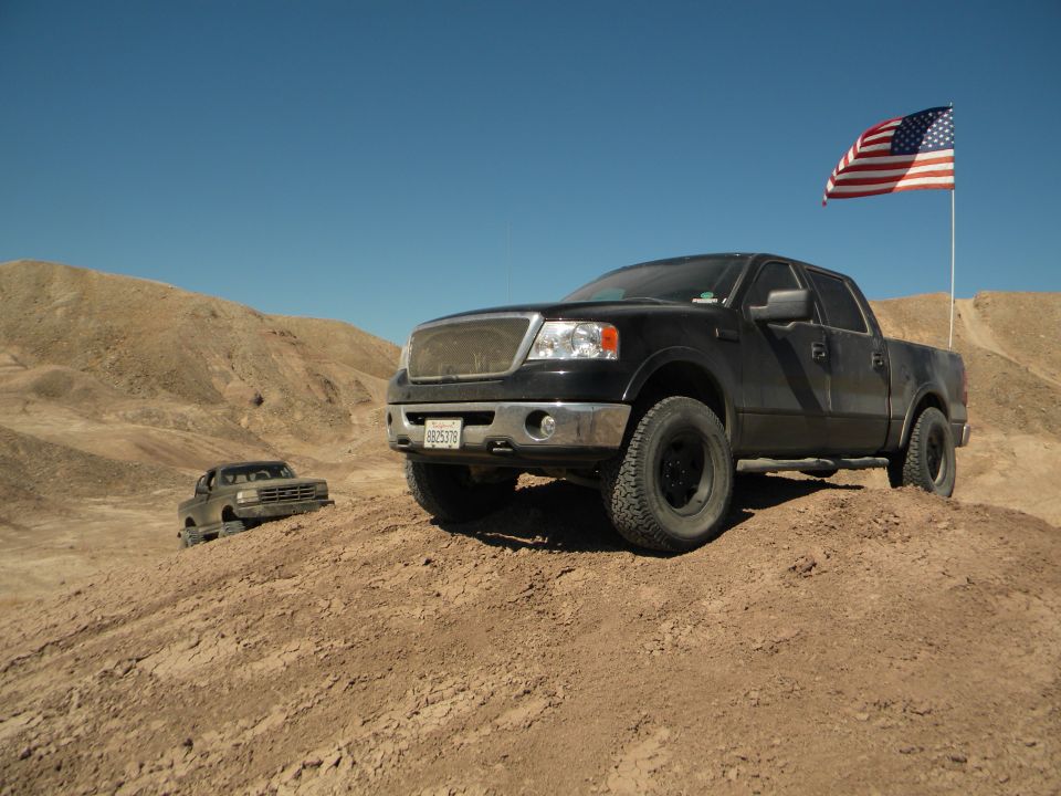 Black pickup truck with American flag flying in desert landscape