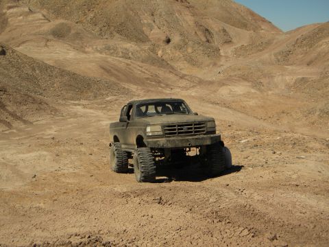 1992 Ford Bronco - Modified 1992 Ford Bronco navigating a dusty, arid terrain with steep hills in the background.