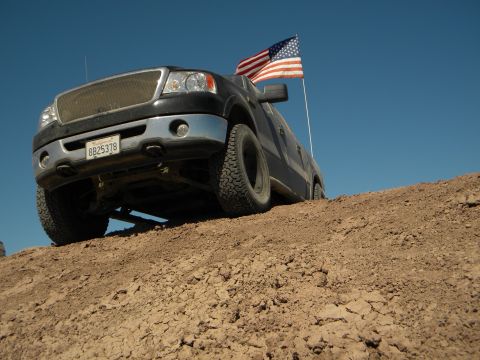 1992 Ford Bronco - A black Ford F-150 pickup truck is shown on a dirt incline with an American flag flying from its antenna.
