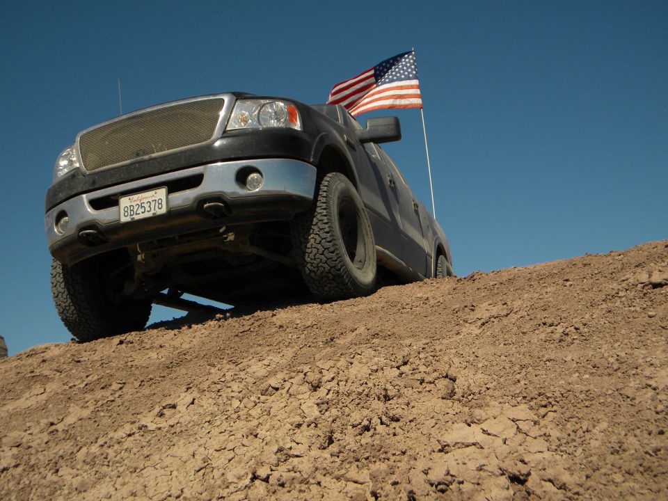 Black Ford F-150 pickup truck with American flag on a dirt hill