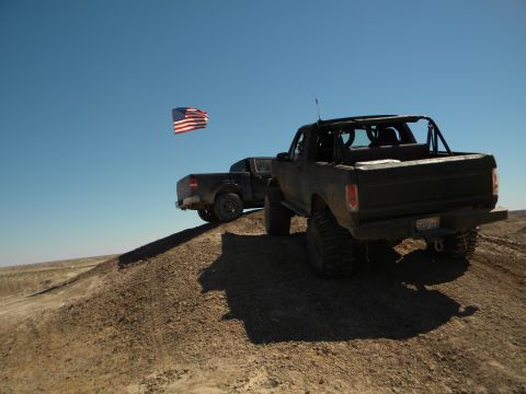 1992 Ford Bronco - Two trucks ascend a dirt hill under a clear blue sky, with an American flag flying.