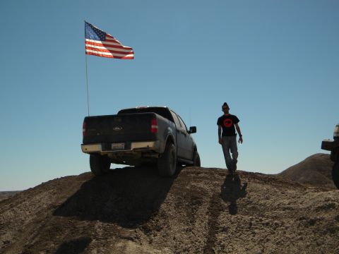 1992 Ford Bronco - Ford F-150 pickup truck flying an American flag on a dirt hill with a person walking nearby.