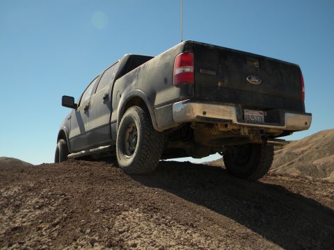 1992 Ford Bronco - Dark-colored Ford F-150 pickup truck navigates a dirt incline under a clear blue sky.