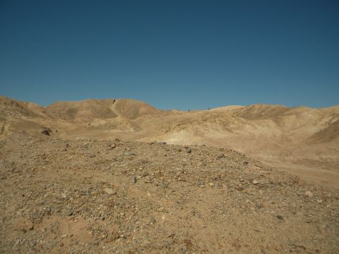 1992 Ford Bronco - A wide view of a barren, rocky desert landscape with rolling hills under a bright blue sky.