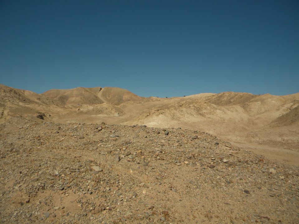 Desert hills and rocky ground under a clear blue sky. Supermotors logo in the corner