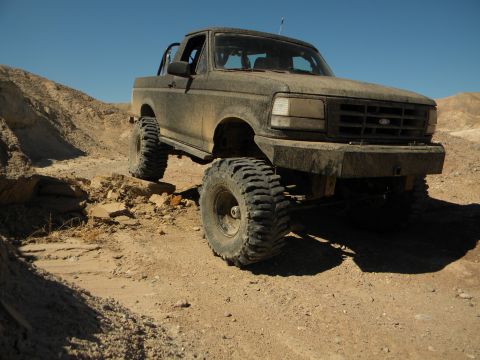 1992 Ford Bronco - This 1992 Ford Bronco is shown in a three-quarter front view, covered in mud and navigating rough terrain.