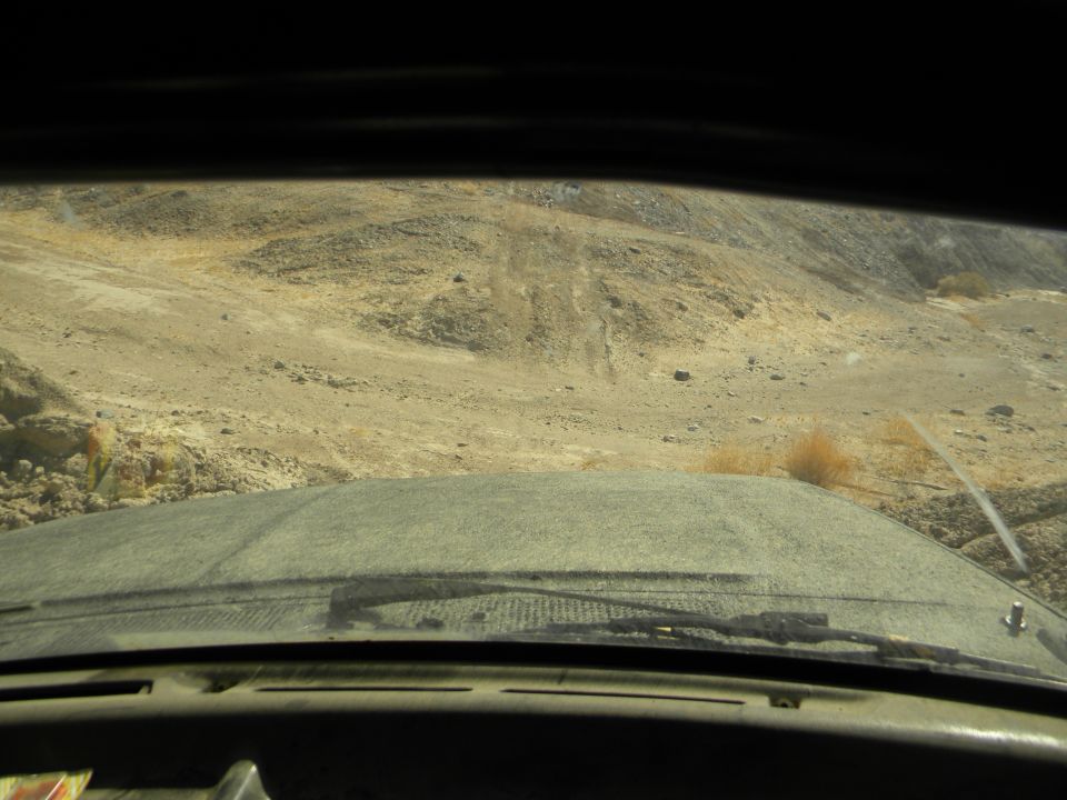 View from inside a dusty vehicle driving on a dirt road in a desert landscape