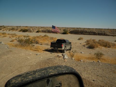 1992 Ford Bronco - A lone pickup truck is parked in a dry, dusty landscape with an American flag waving in the background.