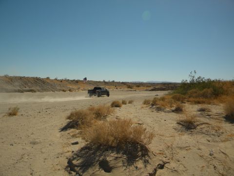 1992 Ford Bronco - A truck drives down a dusty desert road under a clear blue sky.