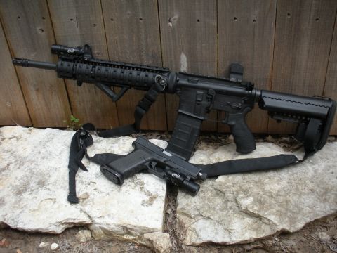 1996 Ford Bronco - Two firearms, an assault rifle and a handgun, are displayed on a rocky surface in front of a wooden fence.