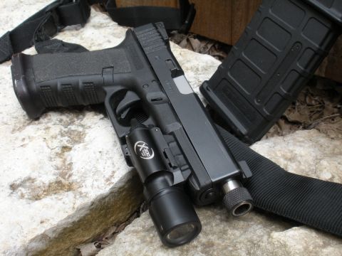 1996 Ford Bronco - A pistol equipped with a tactical light and an extended magazine rests on a rocky surface.