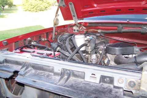 1990 Ford Bronco - Engine bay of a 1990 Ford Bronco, with the hood open, revealing the battery and engine.