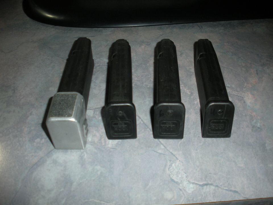Four black gun magazines, one with a silver base, arranged on a tiled surface