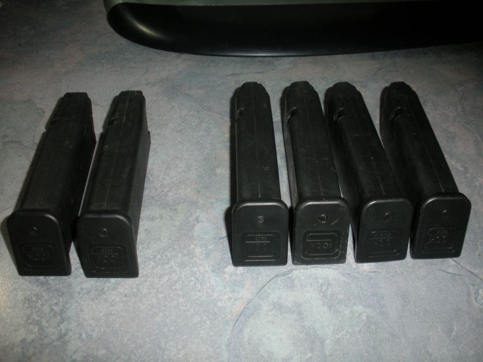 six black gun magazines on a gray surface, two on the left and four on the right