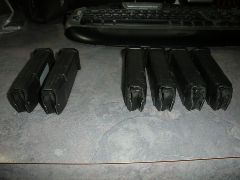 Six black gun magazines on a gray speckled surface, with a keyboard in the background. The magazines are arranged in two groups of two and four