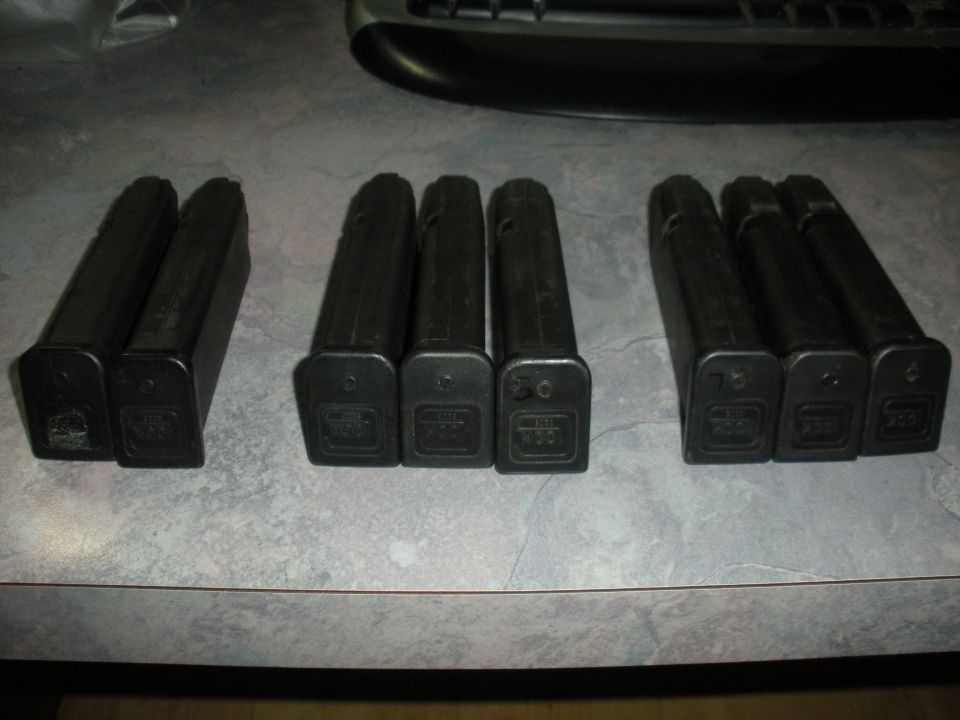 Eight black gun magazines with Glock logos on a speckled surface