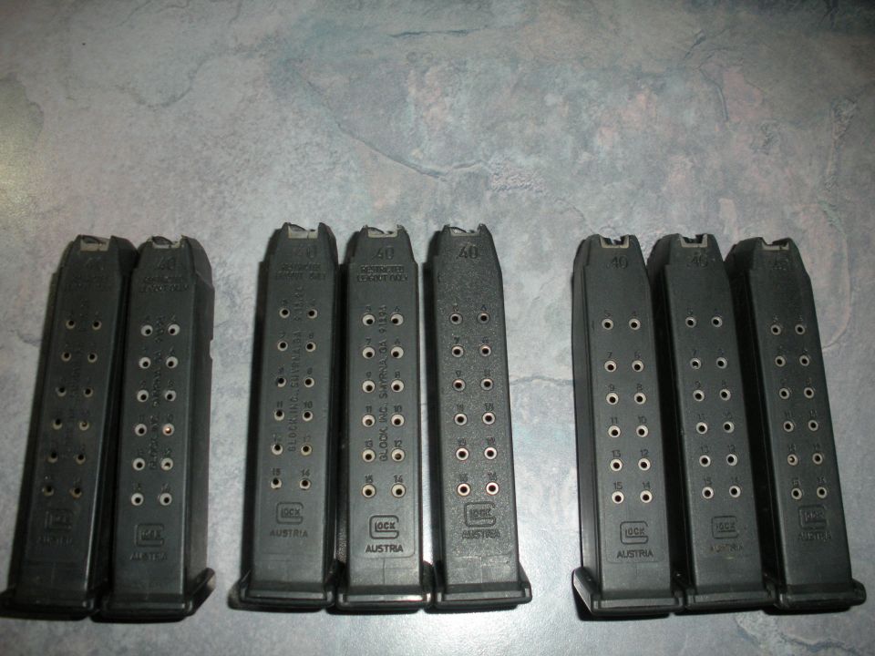 Eight black Glock magazines arranged in two rows on a textured surface