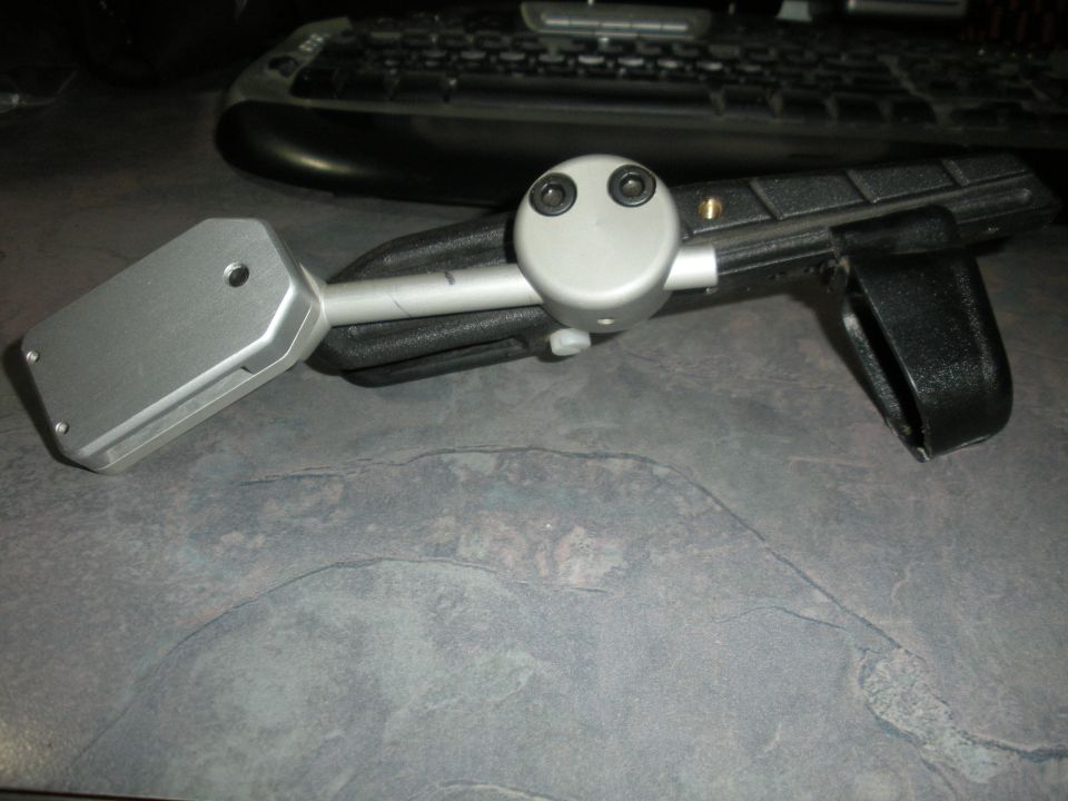 Silver automotive part with black strap and two black screws on a gray surface