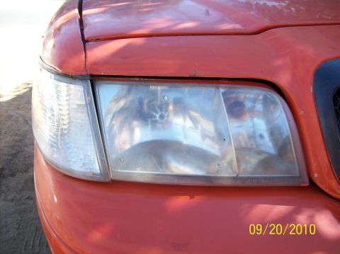 2002 Ford Crown Victoria - Close-up of the front headlight on a red 2002 Ford Crown Victoria.