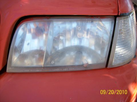 2002 Ford Crown Victoria - Headlight assembly on a red vehicle, with visible text on the lens.
